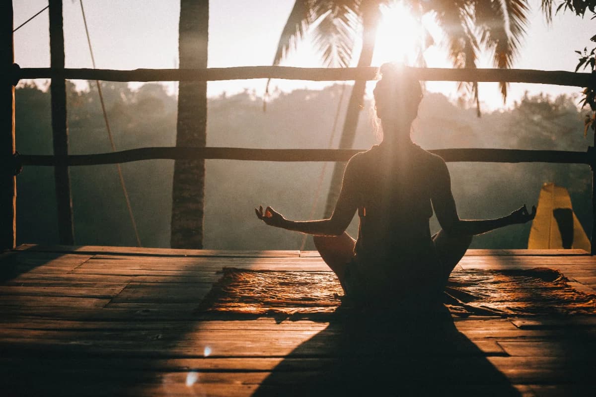 Une femme assise en méditation sur une terrasse en bois au lever du soleil, face à la jungle costaricienne